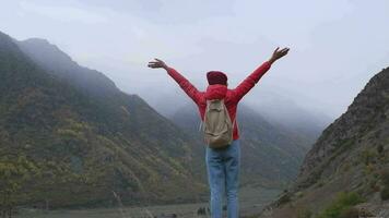 une femme voyageur dans une brillant veste avec une sac à dos dans le montagnes dans l'automne, profiter le vue de le brumeux Caucase montagnes. montagnes et paysage, Voyage à le Caucase montagnes video