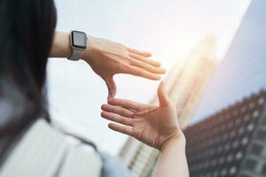 Businesswoman hand gesture focusing on search frame with tall buildings, business city area showing view of approaching target. Concept of vision and strategic planning photo