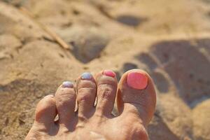 Woman's toes with broken pedicure nails on beach sand photo