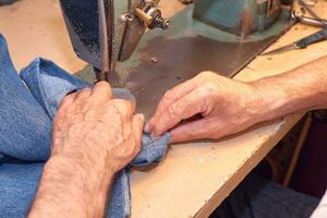 Hands of a tailor sewing blue jeans on a sewing machine photo