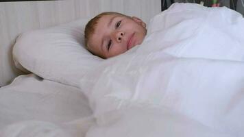 porträtt av en Lycklig söt rolig glad liten pojke i grå pyjamas i säng, ser på de kamera och skrattande video