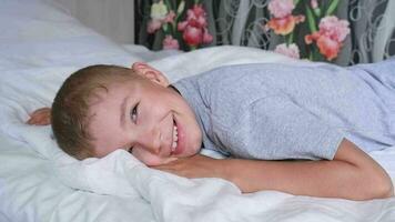 Cute eight year old happy boy smiling in bed and having fun at home on a sunny morning. video