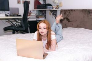 young woman lying with laptop on bed at home photo