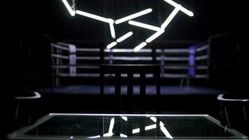 Boxing ring and two chairs with table dark background. View of a regular boxing ring surrounded by blue ropes spotlit by a spotlight. Light show around the boxing ring. photo