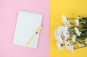 A clean notebook and pen on a light pink table. Mockup with a bouquet of flowers on a yellow table photo