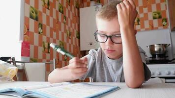 stanco triste poco bambino ragazzo si siede a un' tavolo nel il cucina e scrive compiti a casa. noioso Lezioni video