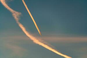 avión volador con condensación caminos o estela en el cielo en el puesta de sol foto