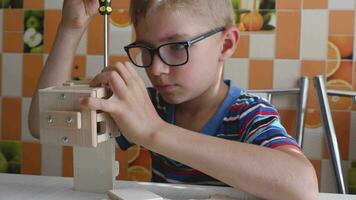 Portrait of a 7-8 year old boy with a screwdriver, carefully assembling a wooden car, sitting at the kitchen table. hands close up. video