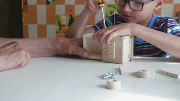 A five-year-old boy independently assembles a wooden construction kit with a screwdriver. Hands close-up video