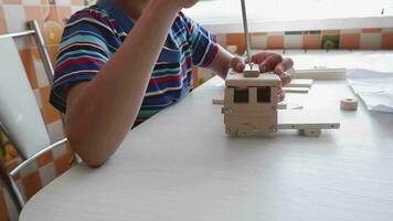 An 8-year-old boy assembles a wooden constructor by himself with a screwdriver. Close-up hands video