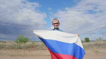 retrato do uma bonitinho, sorridente feliz Garoto dentro uma campo com uma russo bandeira em dele ombros. nacional feriado independência dia. orgulho e patriotismo video