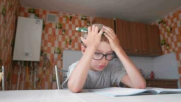 müde traurig wenig Kind Junge sitzt beim ein Tabelle im das Küche und schreibt Hausaufgaben. langweilig Lektionen video