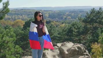 ein Brünette Mädchen mit ein Russisch Flagge gegen das Hintergrund von ein schön Landschaft von das Kaukasus Berge. Russisch Unabhängigkeit Tag video