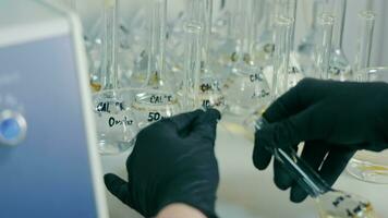 Laboratory studies of a new virus. Many flasks with yellow liquid are on the laboratory table, a laboratory assistant in black gloves takes one flask and brings it to the apparatus with a tube. Close video