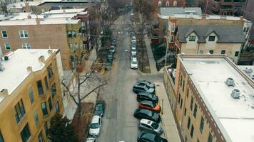 Aerial flying in the city over the road with cars. Cars are parked of the road next to residential buildings. It's autumn time, a row of parked cars near the houses. Cars are parked on both sides of video