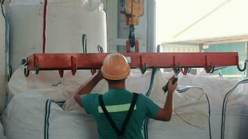 trabajador operando grua a levantar pesado sacos en depósito. almacén trabajador en la seguridad engranaje operando un gastos generales grua a maniobra grande sacos video