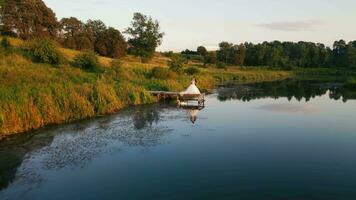 das Braut und Bräutigam sind Stehen durch das See auf das Brücke und ein Schwan ist Schwimmen in der Nähe von Sie beim Sonnenuntergang. Schwan Paar Jungvermählten. Betrachtung von ein jung Paar im das See. Grün Park auf das Horizont video