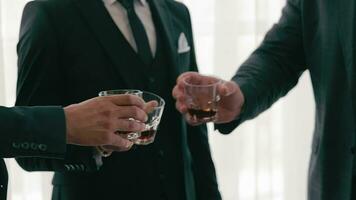 de cerca de masculino manos participación lentes de whisky, coñac, brandy. un empresa de negocio hombres en trajes tintinamente lentes de whisky en su manos. video