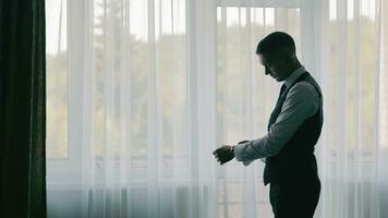 Caballero preparando para evento, silueta de un hombre en traje ajustando su manga por un ventana con escarpado cortinas video