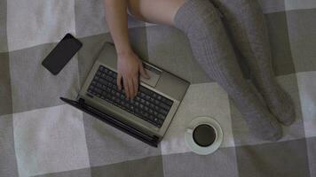 Overhead shot, young creative business girl working using laptop and mobile phone sitting on the bed at home. Nearby is a cup of coffee. 4K video