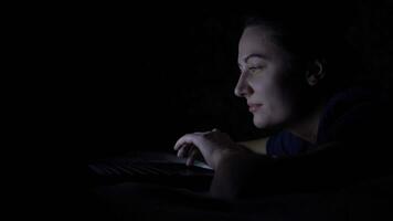 Attractive happy woman is using a mobile computer while lying on a bed at night. Isolated light 4K video