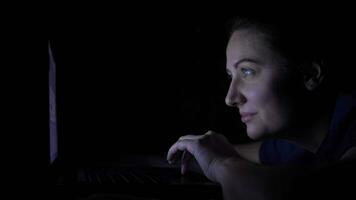 Attractive young girl is using mobile computer while lying on the bed at home at night. Isolated light 4K video