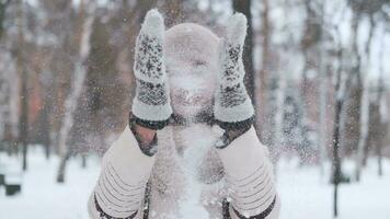 beautiful young woman with dark hair and blue eyes in a hat and scarf in a winter park claps mittens snow smiles and is very happy. slow motion video