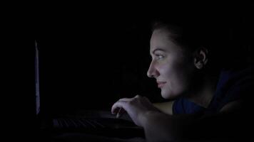 A young girl is using a mobile computer while lying on a bed at home at night. Isolated light 4K video