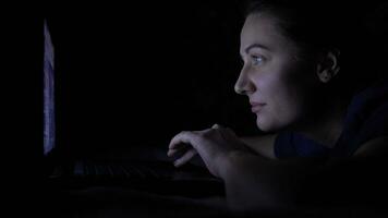 An attractive young girl is using a mobile computer while lying on a bed at night. Isolated light 4K video