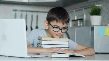 un colegial en lentes lo hace deberes mientras sentado en el cocina a el mesa utilizando muchos libros de texto retrato de un colegial video