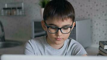 Portrait of an attractive boy in glasses who does homework using a laptop. video