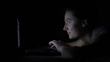 atractivo hermosa joven mujer acostado en el cama utilizando un ordenador portátil en un oscuro habitación video