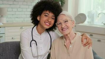 afro americano donna medico e paziente anziano donna seduta su divano e sorridente. famiglia medico, paziente sostegno, Aiuto a casa, cura per il malato. video