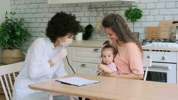 afro américain femme médecin examine peu fille à Accueil tandis que séance à table dans cuisine. famille médecin, patient soutien, Aidez-moi à maison, soins pour le malade. video