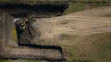 Excavating dirt into a dump truck to build a water storage pond for use in the dry season for agriculture. Aerial view of a backhoe is working. video