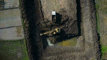 escavação sujeira para dentro uma despejo caminhão para Construir uma água armazenamento lagoa para usar dentro a seco estação para agricultura. aéreo Visão do uma retroescavadeira é trabalhando. video