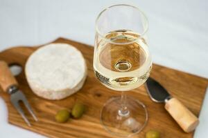 A wineglass of white dry wine and in camembert cheese on a wooden board. Close-up. Selective focus. photo