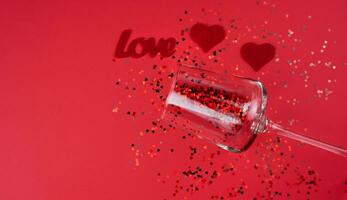 A two red hearts, word LOVE and small red hearts in wineglass on the red background. Valentine's Day concept. Banner. Top view. Copy space. Selective focus. photo