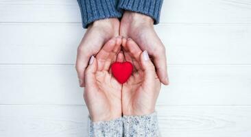 Woman's and man's hands holds red heart on white wooden background. Close-up. Top view. Place for text. photo