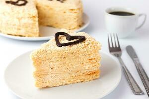 un pedazo de pastel Napoleón en un blanco plato y un taza de café en el antecedentes. sabroso desayuno. de cerca. selectivo enfocar. foto