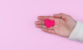 Woman's hands hold a pink heart on a pink background. Banner. Copy space. Top view. Selective focus. photo