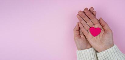 Woman's hands hold a pink heart on a pink background.Valentine's Day composition. Banner. Place for text. Top view. Selective focus. photo