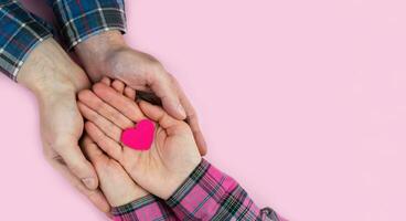 mujer y del hombre manos sostener un rosado corazón en un rosado antecedentes. el concepto de amar, familia y amistad. bandera. parte superior vista. sitio para texto. selectivo enfocar. foto