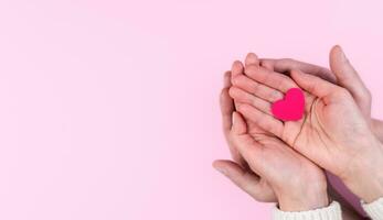 Woman's and man's hands hold a pink heart on a pink background. The concept of love, family and friendship. Banner. Top view. Flatlay. Selective focus. photo