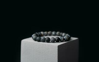 Natural stone bracelet on a gray podium on a black background. Close-up. photo