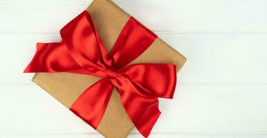 Gift box with red ribbon bow on white wooden background. Copy space. Close-up. Top view. Flatlay. photo