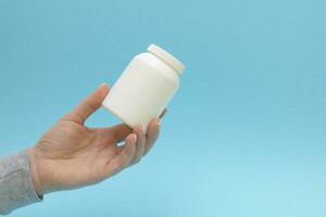 the pill bottle, medicine container for vitamins in female hand on blue background. photo