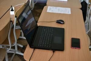 un negro ordenador portátil y un teléfono en el escritorio. un oficina lugar de trabajo con un computadora. foto