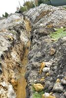 A plastic black gas pipe at the bottom of the trench. A dug trench for laying a gas pipe. photo