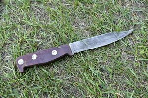 A homemade knife on the grass. An iron knife with a handle. photo